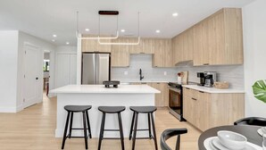 Une cuisine moderne dotée d’un îlot central, de tabourets de bar et d’un coin repas avec une table et des chaises.