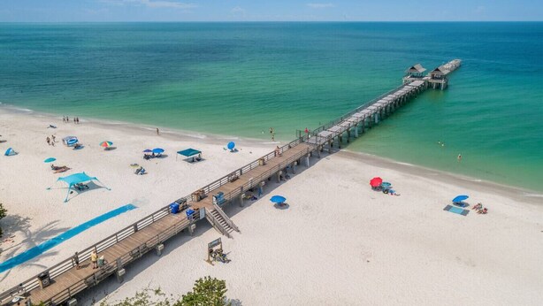 Une plage avec une jetée en bois qui s’avance dans l’océan, agrémentée de parasols et de chaises longues.
