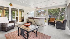 Een ruim terras met rieten meubilair, een jacuzzi en een grote glazen deur die uitkomt op een achtertuin.