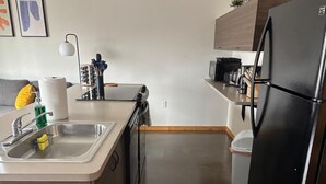 Een moderne keuken met een RVS spoelbak, een zwarte koelkast en houten keukenkastjes.
