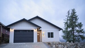 A modern two-story house with a garage, stone wall, and a large pine tree.