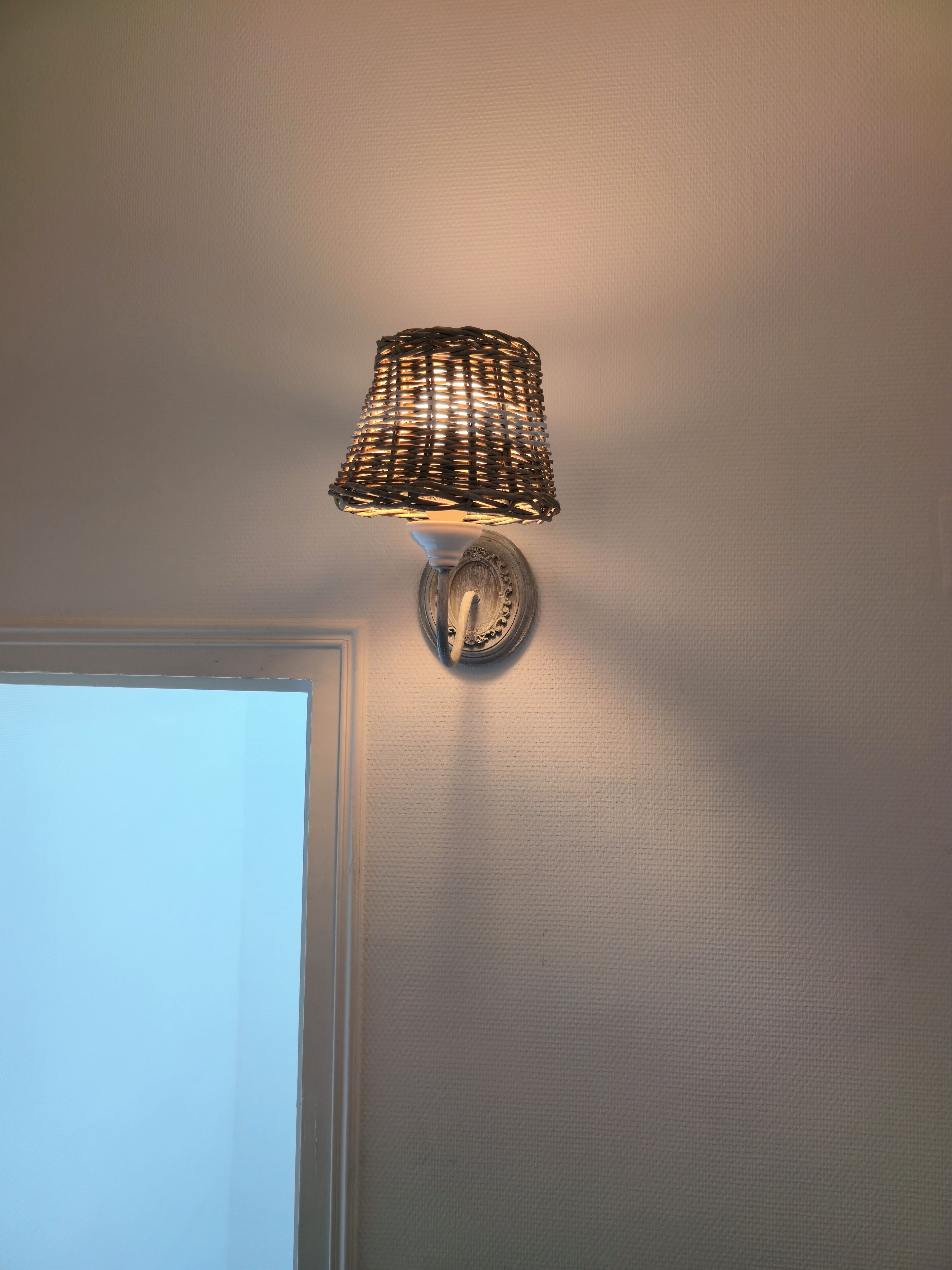 A wall-mounted lamp with a woven shade and a decorative base.
