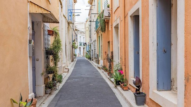 A narrow street lined with buildings, some with balconies and potted plants. - The discreet 18th century (Sérignan)
