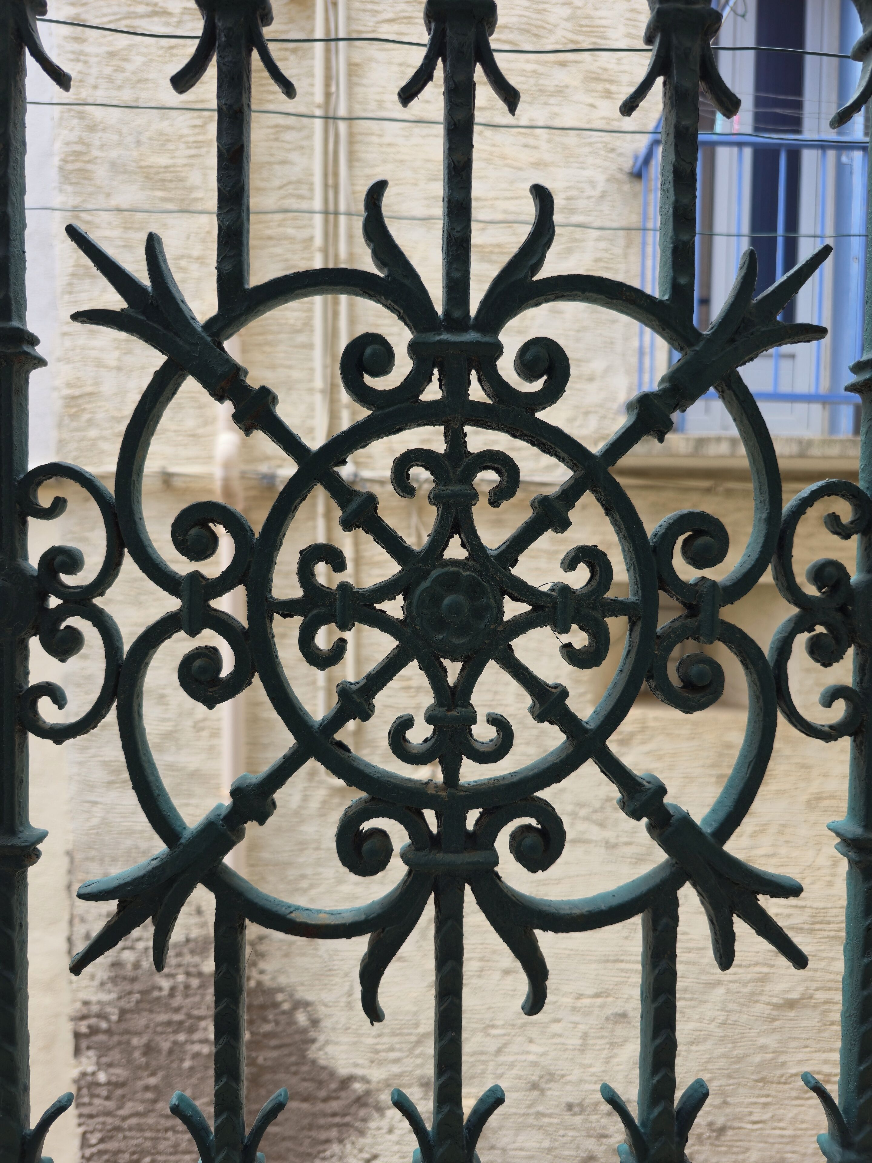 A wrought iron gate with intricate designs, featuring a central circular motif and flanked by vertical bars.