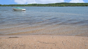 Un bote en un lago tranquilo, con una playa arenosa y una colina boscosa al fondo.