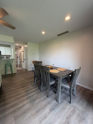 Un comedor con mesa y sillas de madera, una cocina al fondo y un pasillo que conduce a otra habitación.