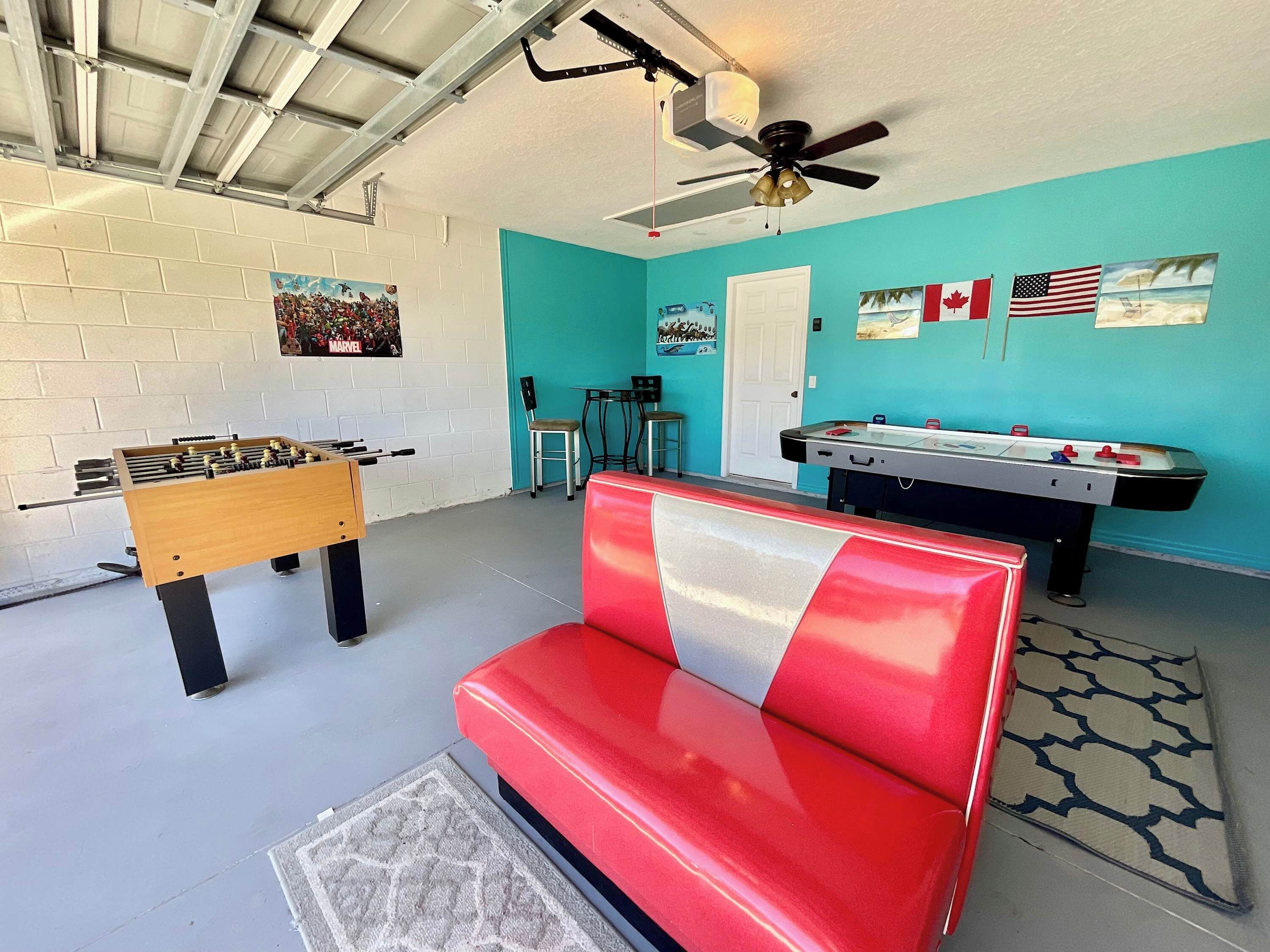 Une pièce avec un baby-foot, une table de billard, un banc rouge et un ventilateur de plafond.