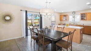 A dining area with a dark wooden table and chairs, a chandelier, and a view through the glass door to the outside. - Magic Oasis Retreat (Davenport)