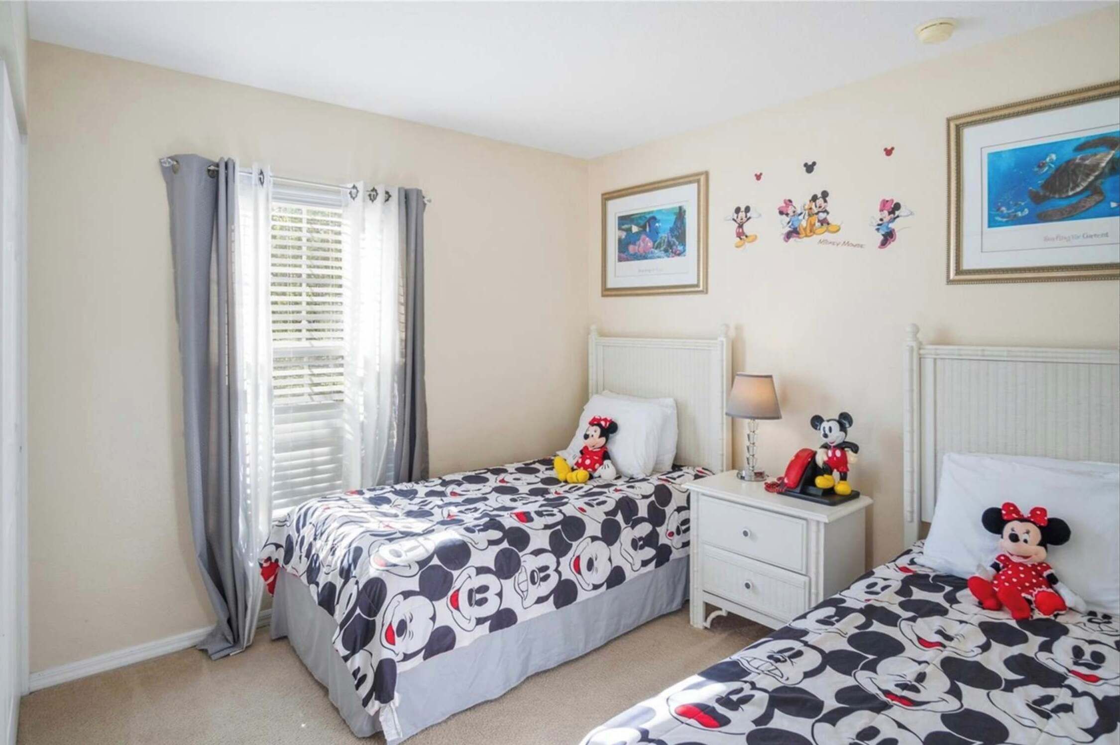 Een slaapkamer met twee bedden, elk met een sprei met Mickey Mouse thema. Er zijn Mickey Mouse decoraties aan de muren en een lijst met een foto van een schildpad.
