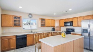 A modern kitchen with wooden cabinets, a stainless steel refrigerator, a dishwasher, and a central island with bar stools. - Magic Oasis Retreat (Davenport)