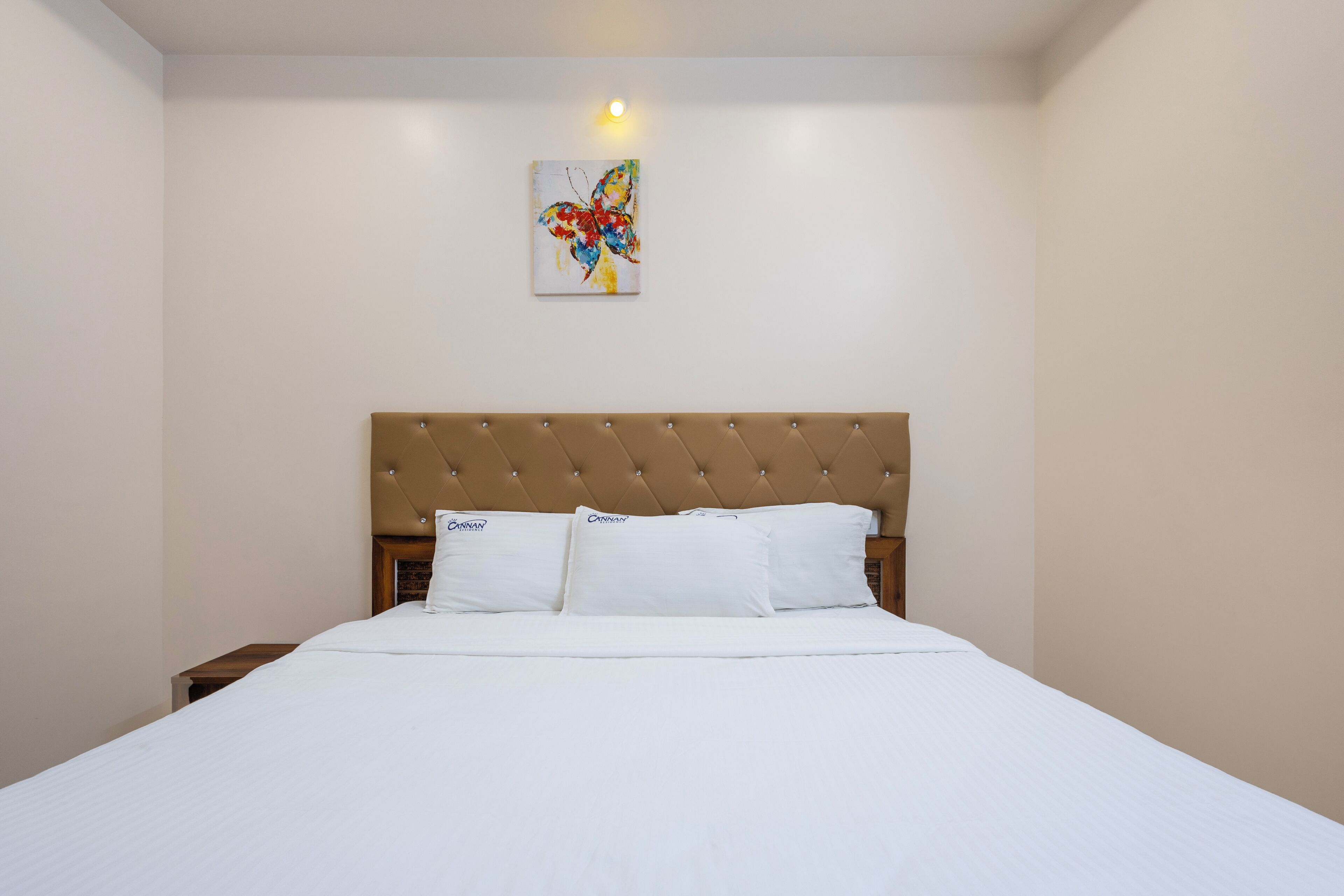 A neatly made bed with a tufted headboard, white bedding, and a single wall-mounted artwork.