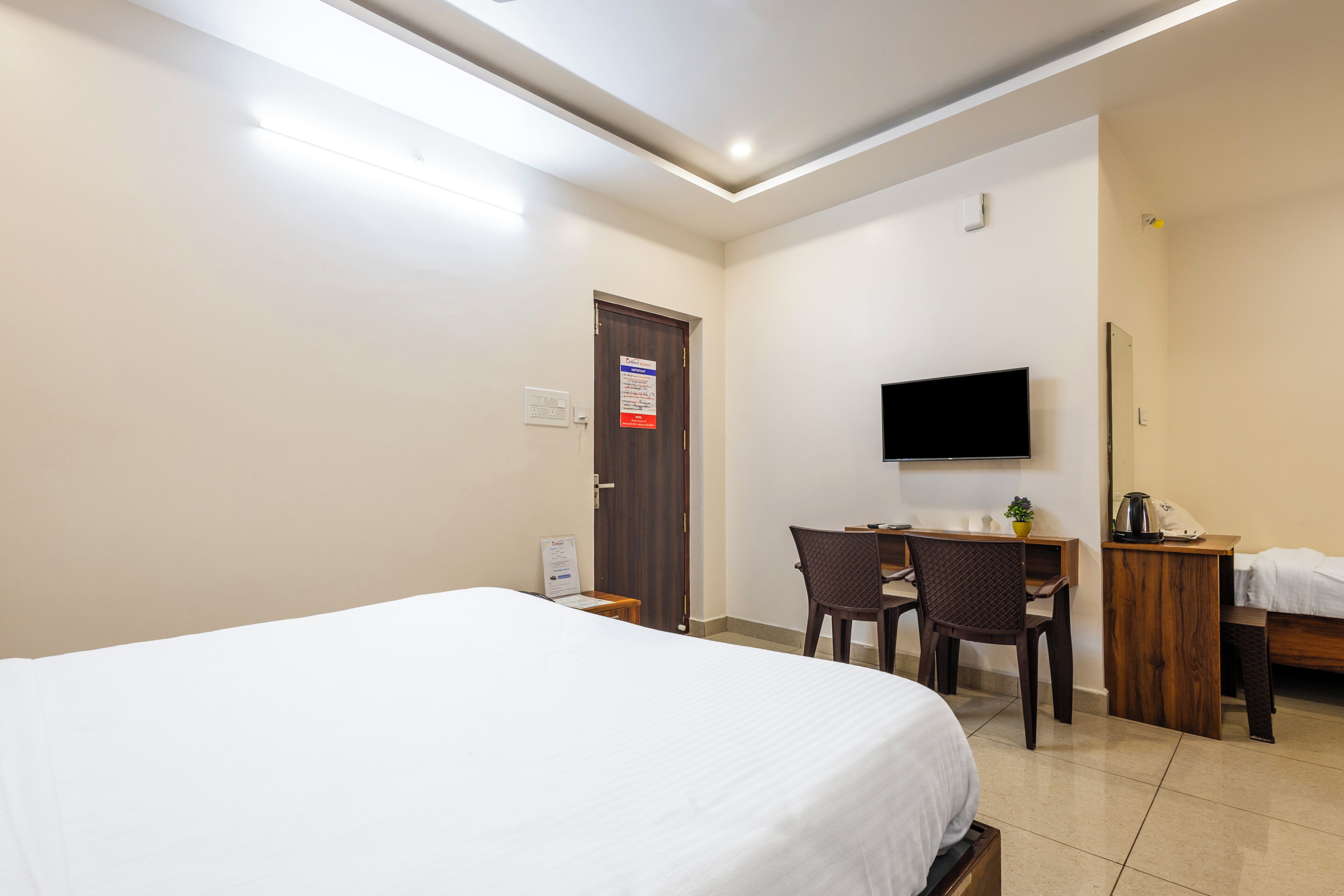A hotel room with a bed, a desk, a chair, a television, and a small table with a plant.
