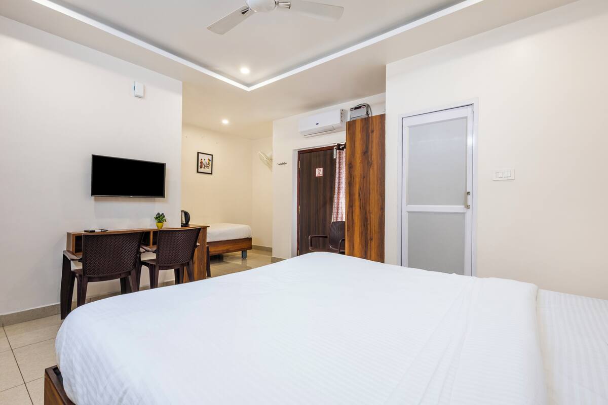 A hotel room with a bed, a desk with chairs, a television, and a wardrobe.
