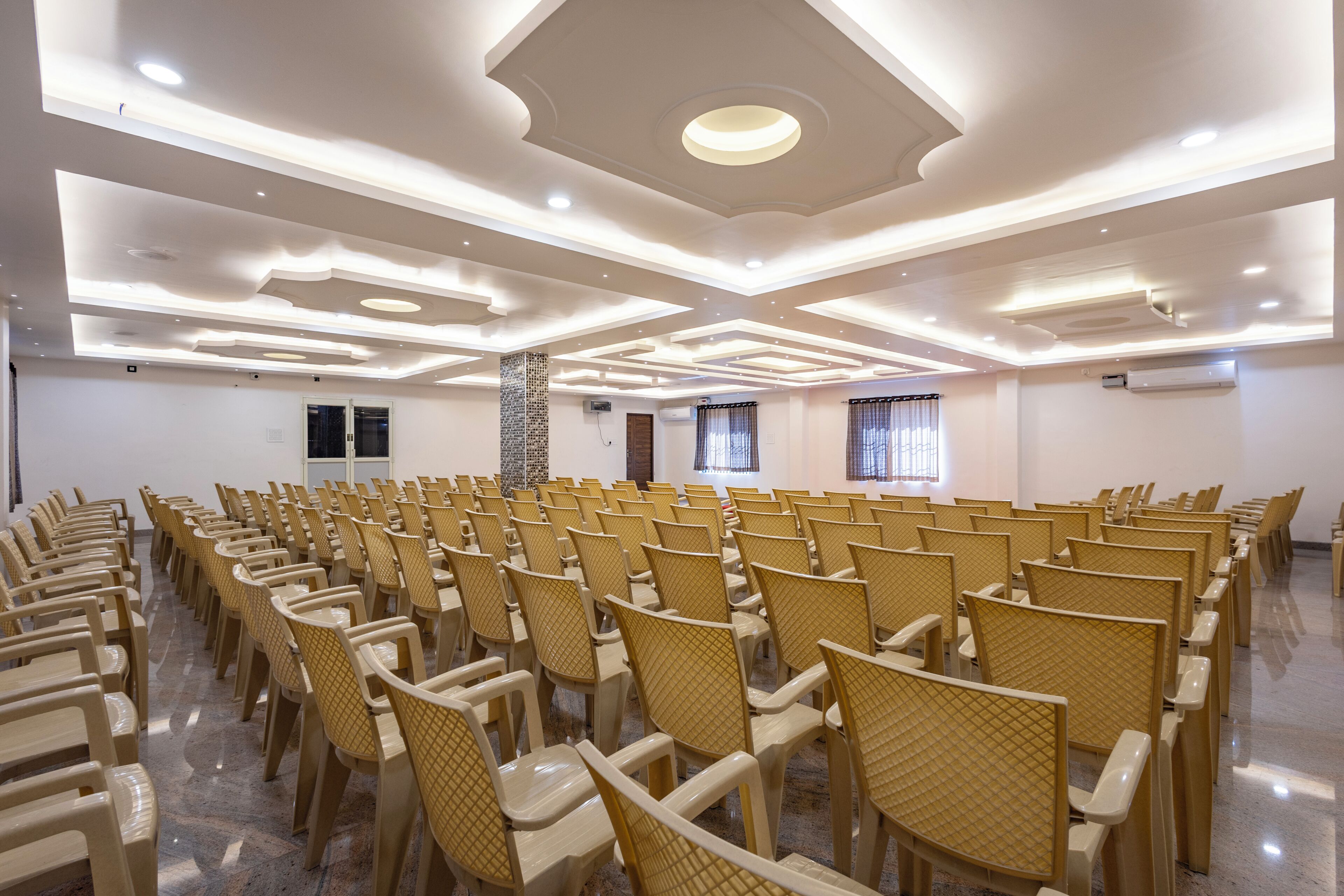 A conference room with rows of chairs, a patterned ceiling, and a door.