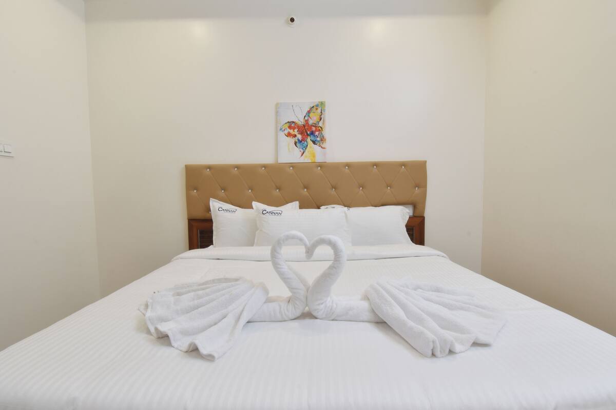 A hotel room with a bed, white linens, a tufted headboard, and a butterfly artwork on the wall.