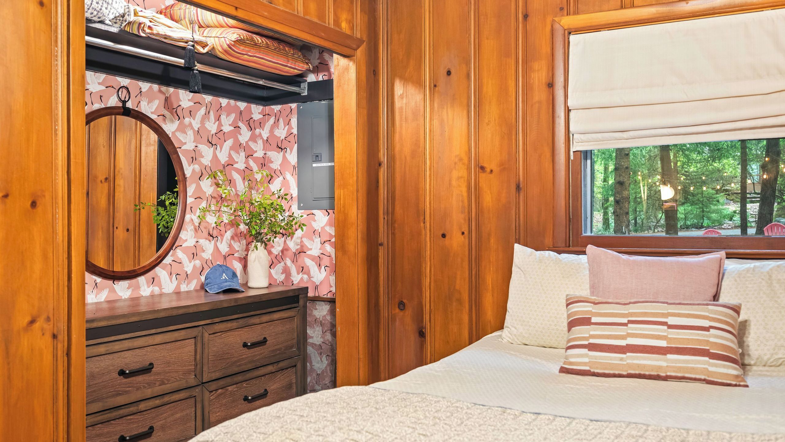 Une chambre à coucher dans une cabane en bois, avec un lit, une commode, un miroir et une fenêtre donnant sur la forêt.