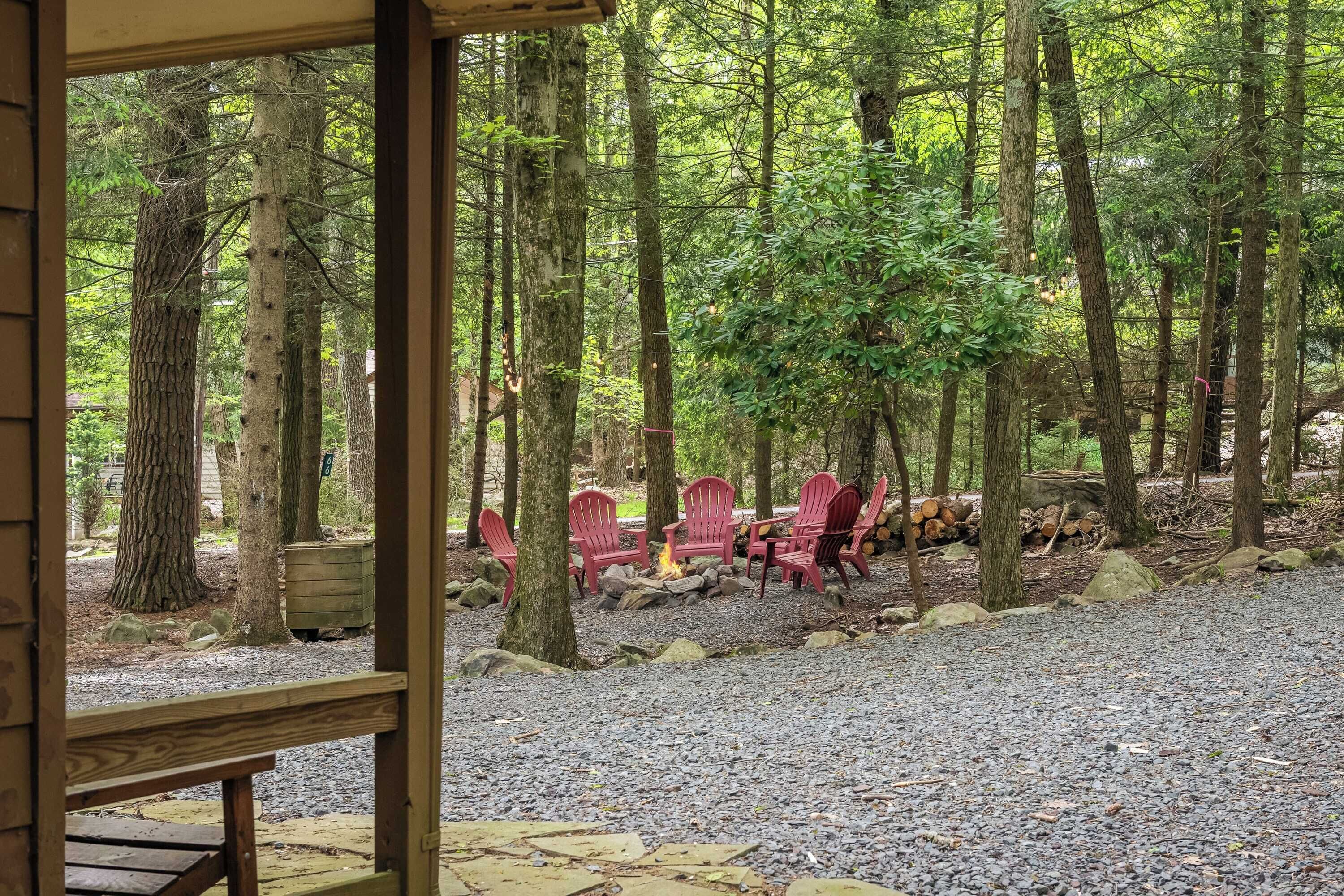 A forested area with a gravel path, red Adirondack chairs, and a fire pit.