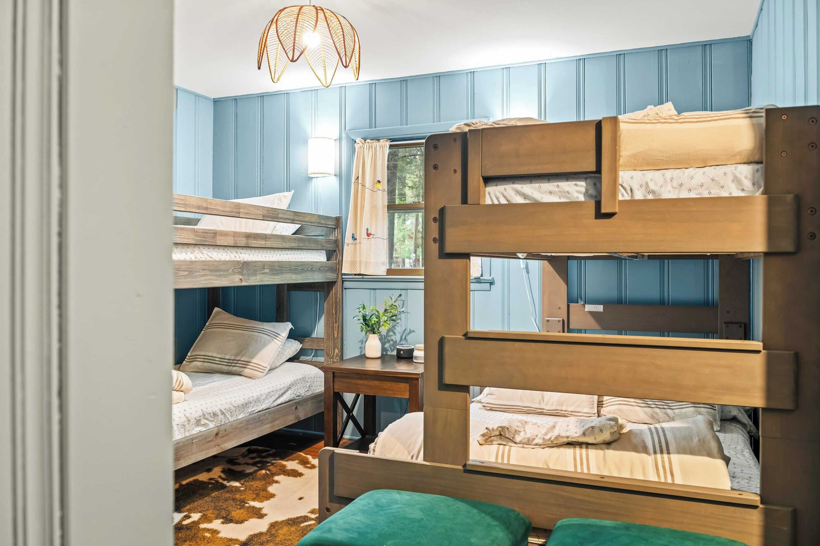 A bunk bed room with a wooden headboard, a small table with a plant, and a window with curtains.