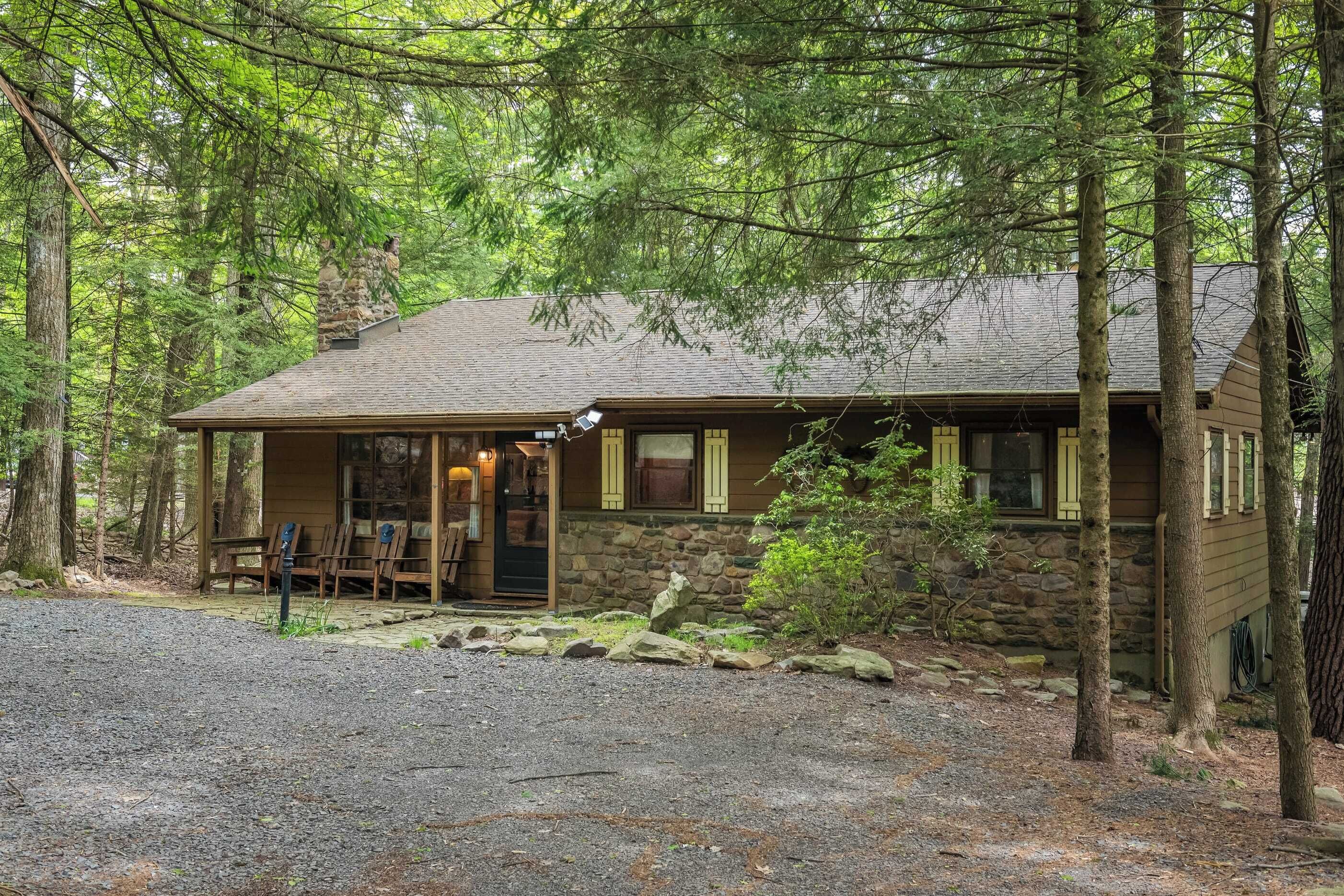 A rustic cabin with a stone foundation, wooden exterior, and a porch with seating.