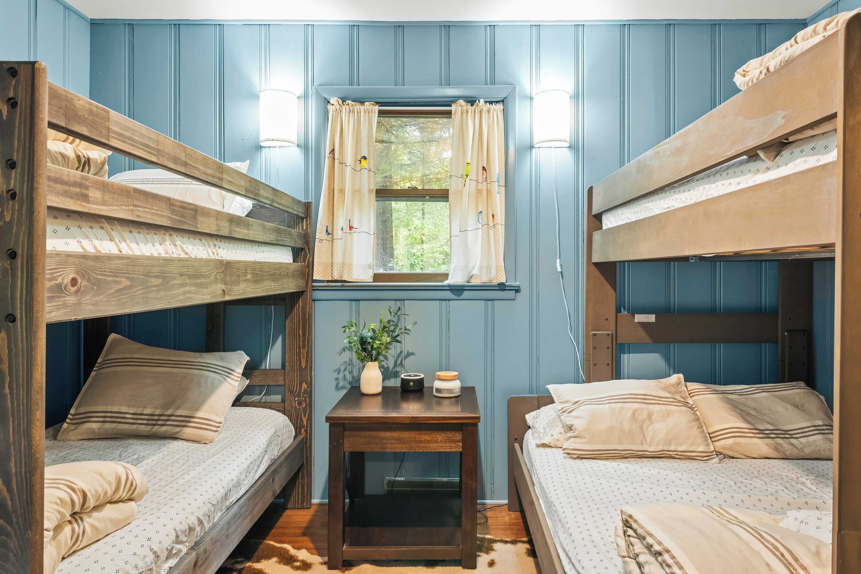A room with bunk beds, a small table with a plant, and a window with curtains.