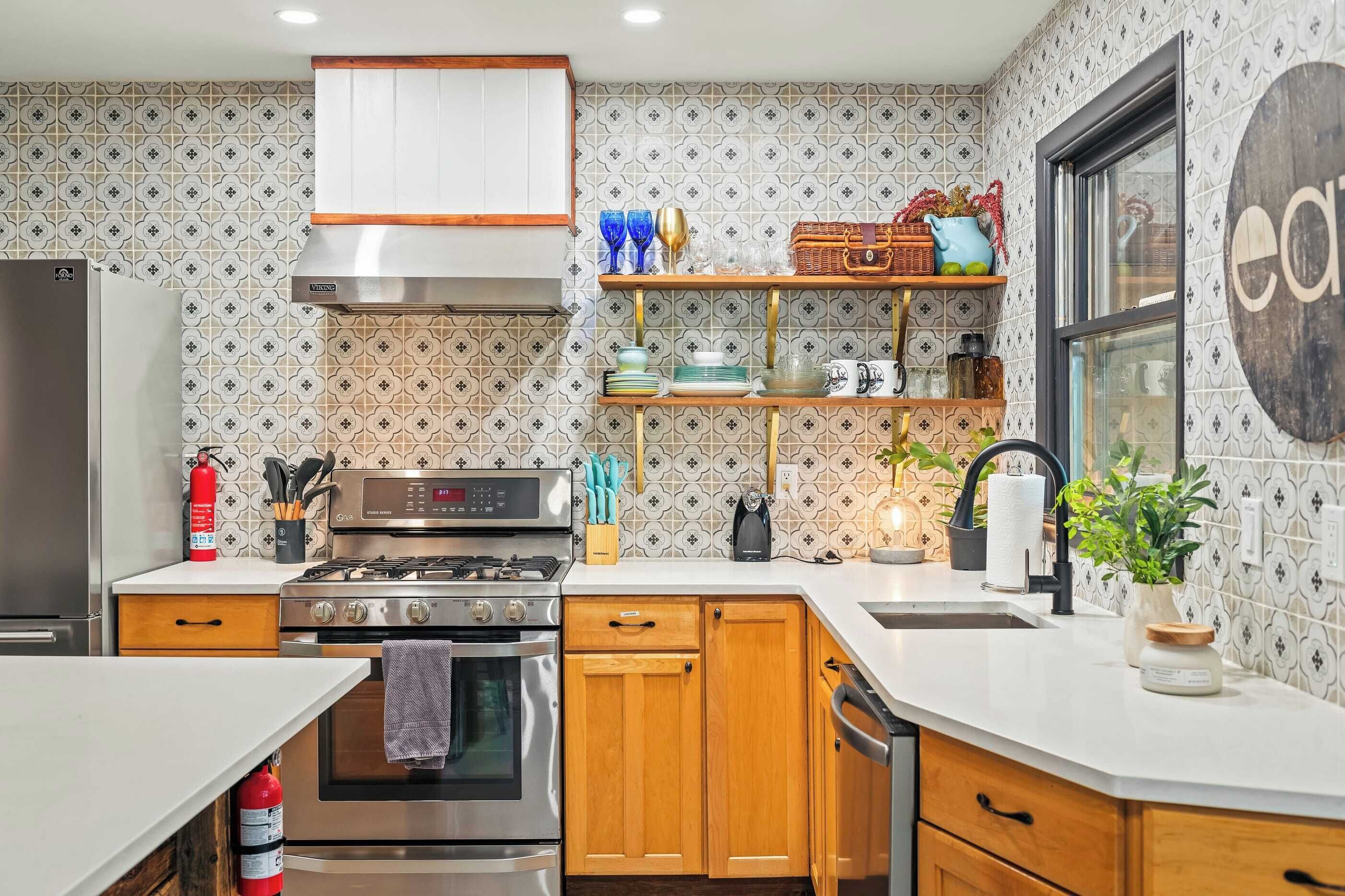 Een moderne keuken met een roestvrijstalen fornuis, houten keukenkastjes en een inbouwoven. Daarboven bevindt zich een houten plank met diverse keukenspullen.