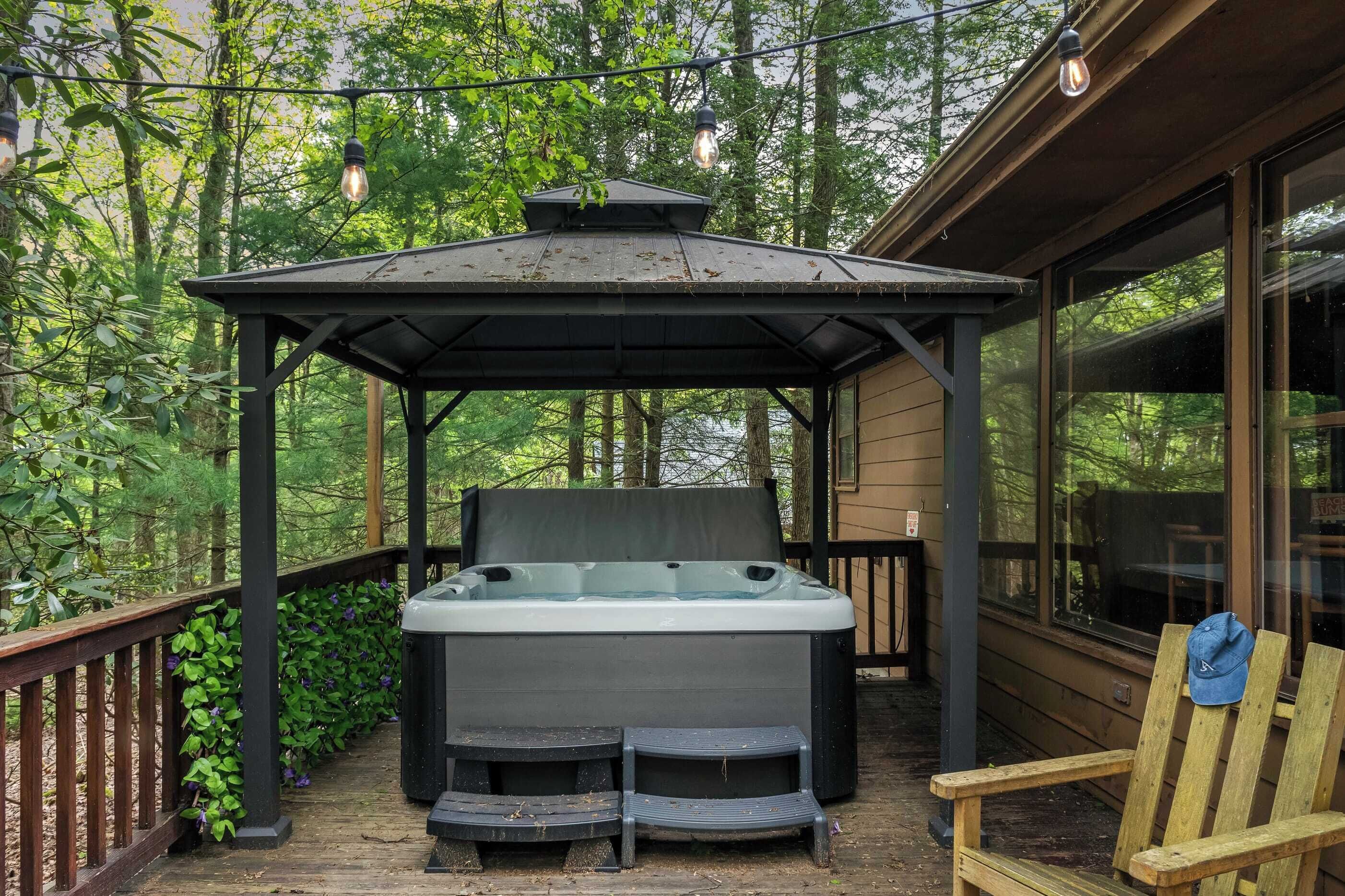 Ein Whirlpool unter einem Pavillon auf einer Holzterrasse, umgeben von viel Grün.