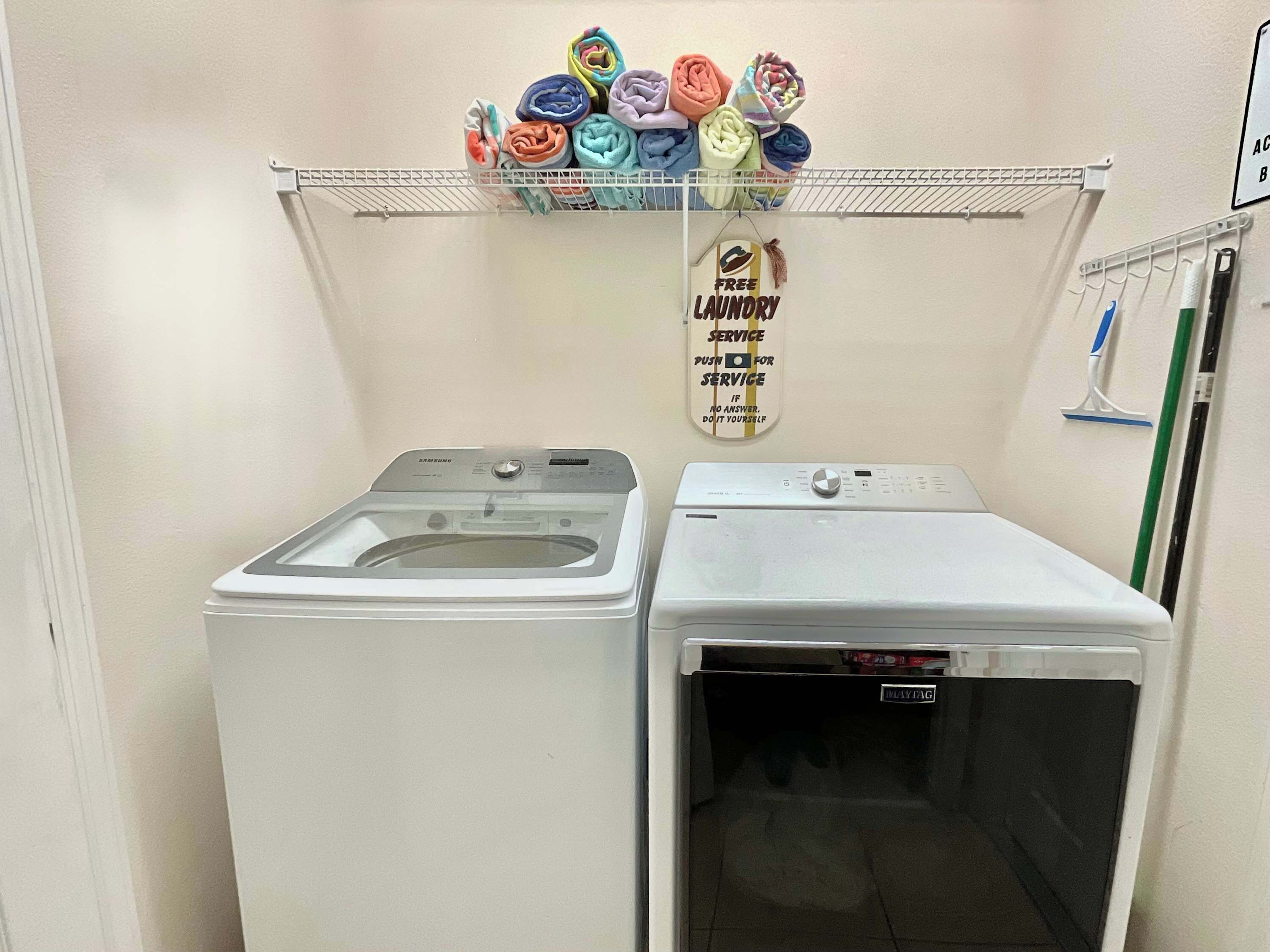 Un espace dédié à la lessive, équipé de deux machines à laver, d’un étendoir avec des vêtements pliés, et d’une affiche proposant un service de blanchisserie gratuit.