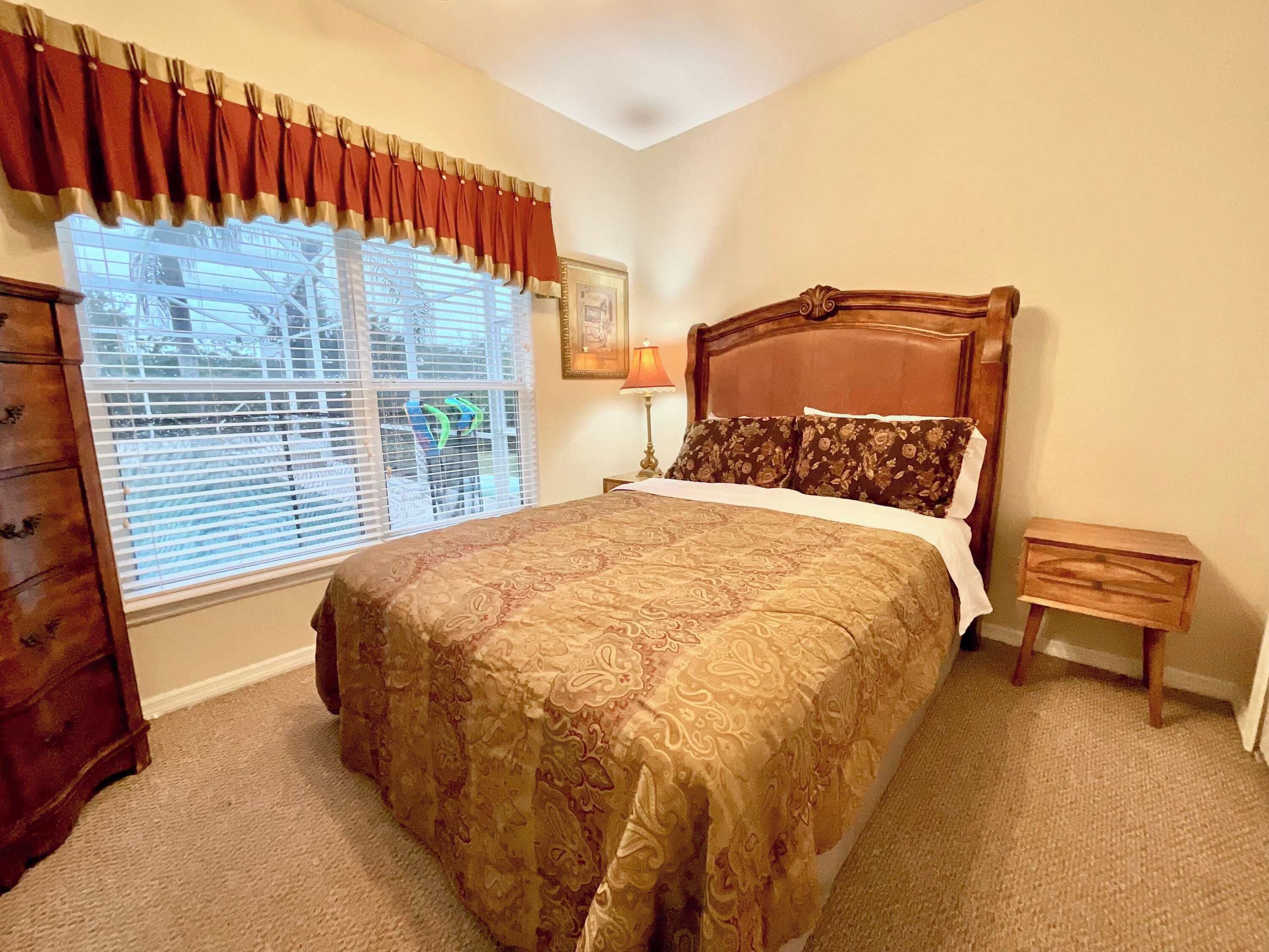 Une chambre à coucher avec un grand lit, une commode, une table de chevet et une fenêtre avec des stores.