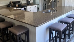 Cozinha com bancada de granito, pia de aço inoxidável e banquetas de madeira escura.