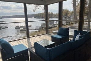 A sunroom with large windows overlooking a lake, furnished with wicker sofas and a glass table. - Beautiful Water Front Homes With Lake/ Dock Access (Creal Springs)