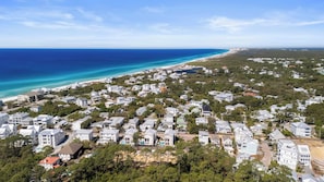 An aerial view of a coastal residential area with houses, a beach, and a clear blue sky.