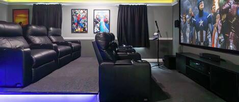 A home theater with leather recliners, a large flat-screen TV, and posters on the wall.