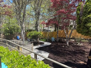 A garden with a wooden deck, a small pond, and various trees. - Relaxing Harwich retreat with beautiful back yard/ pet friendly! (Harwich)