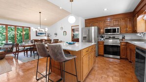 A modern kitchen with wooden cabinets, stainless steel appliances, and a large island with bar stools. - Shady Daze: Waterfront Home w/ Deck, Hot Tub & Lake Views (Sherrills Ford)