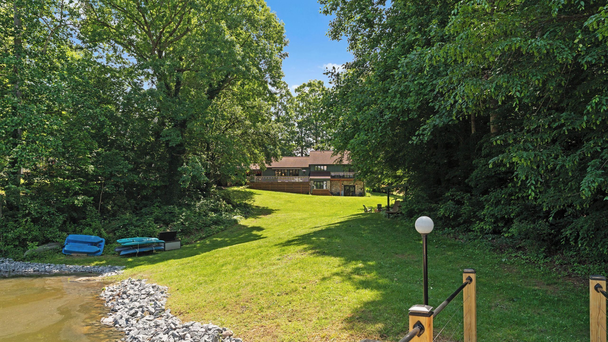 A house surrounded by lush greenery, a grassy yard, and a small pond.