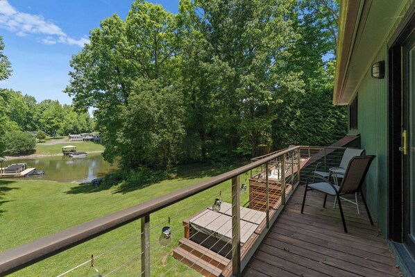 A wooden deck with outdoor seating, overlooking a pond and lush greenery.