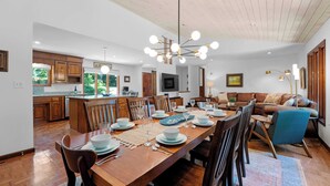 A spacious dining area with a wooden table set for six, surrounded by chairs. A kitchen with wooden cabinets and a large island is visible in the background. - Shady Daze: Waterfront Home w/ Deck, Hot Tub & Lake Views (Sherrills Ford)