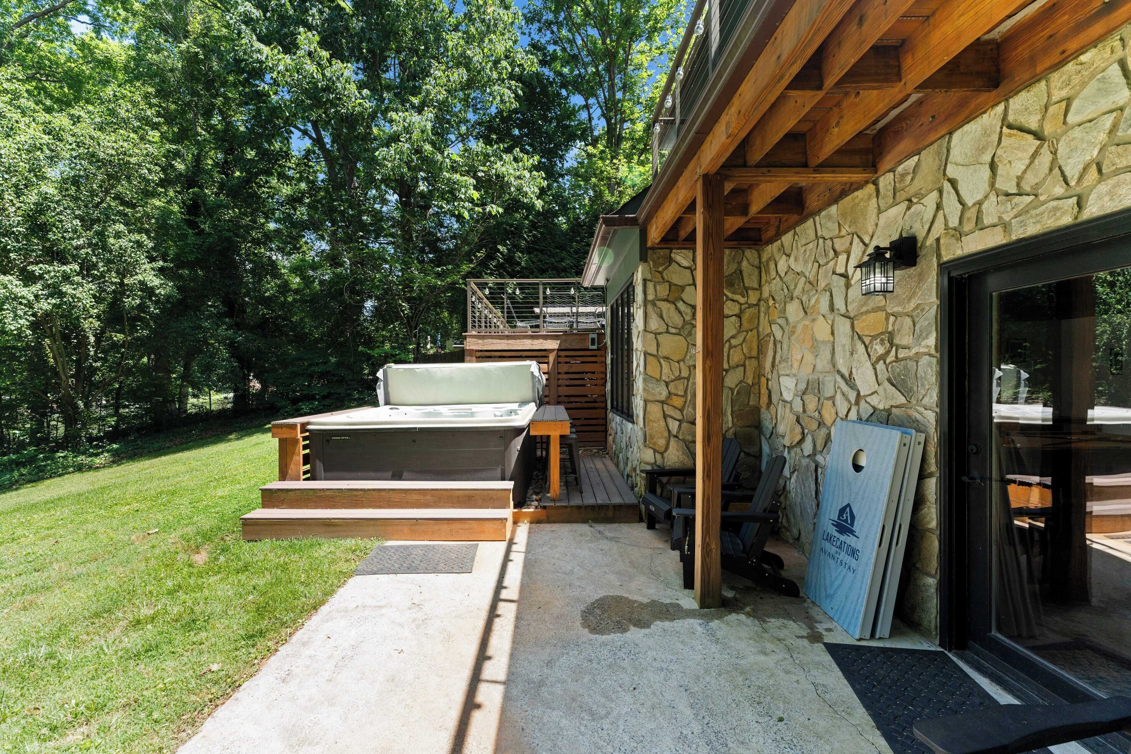 A stone exterior with a wooden deck, outdoor seating, and a hot tub.