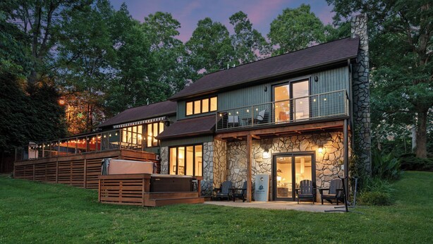 A two-story house with a stone facade, large windows, and a balcony with string lights. - Shady Daze: Waterfront Home w/ Deck, Hot Tub & Lake Views (Sherrills Ford)