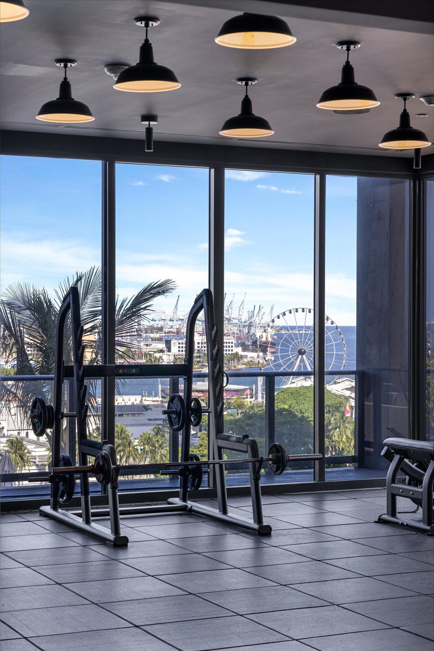 A gym with large windows overlooking a cityscape, including a Ferris wheel.