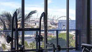 Une salle de sport dotée de grandes fenêtres donnant sur un paysage urbain, avec notamment une grande roue en vue.