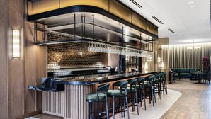 Un espace bar moderne avec un comptoir noir, des tabourets de bar et un mur en briques en arrière-plan.