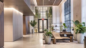 Un hall d’entrée moderne avec un espace salon central, de grandes fenêtres et des plantes en pot.