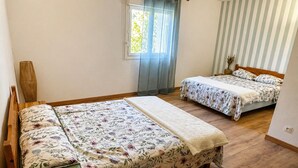 A bedroom with two beds, a window with curtains, and a striped wall.
