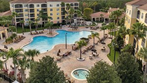 A resort with a large pool, palm trees, and a multi-story building with balconies. - Minutes to Magic (Orlando)