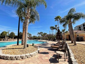 A pool area with palm trees, lounge chairs, and a building in the background.