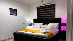 Une chambre à coucher moderne avec une tête de lit noire, du linge de lit blanc, un plaid jaune et un tapis gris.