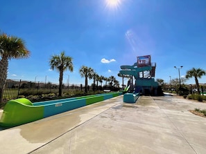 Un parque acuático con una estructura de toboganes de varios niveles, palmeras y un cielo azul despejado.