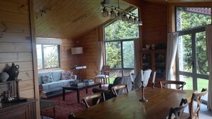 Een gezellig interieur van een chalet met een eethoek, een bank en een groot raam met uitzicht op de omgeving.