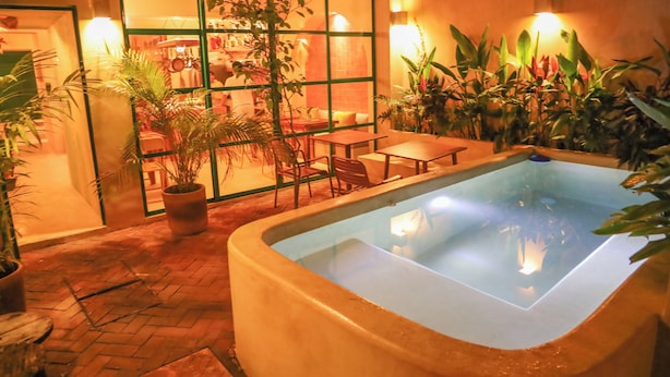 A pool area with a tiled floor, surrounded by potted plants and a seating area with tables and chairs.